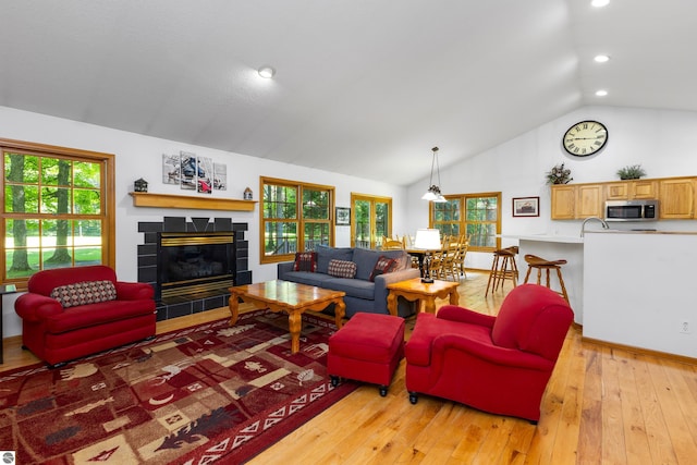 living room with a tiled fireplace, vaulted ceiling, and light wood-type flooring