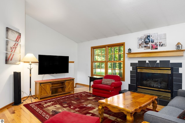 living room with hardwood / wood-style flooring, lofted ceiling, and a tiled fireplace