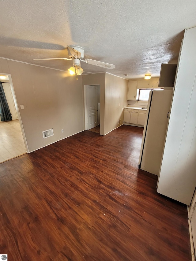 unfurnished living room featuring dark wood-type flooring, a textured ceiling, and ceiling fan