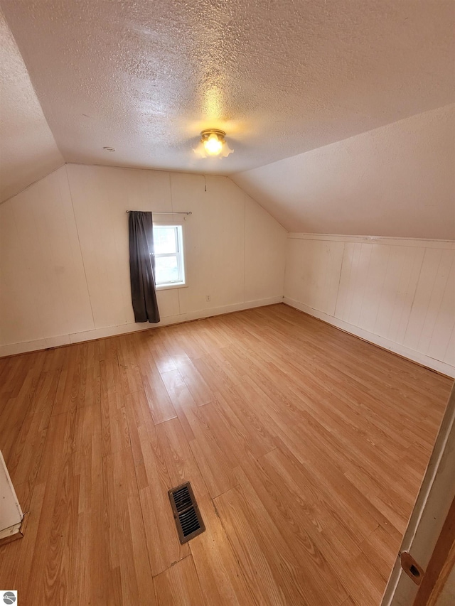 additional living space with lofted ceiling, hardwood / wood-style flooring, and a textured ceiling