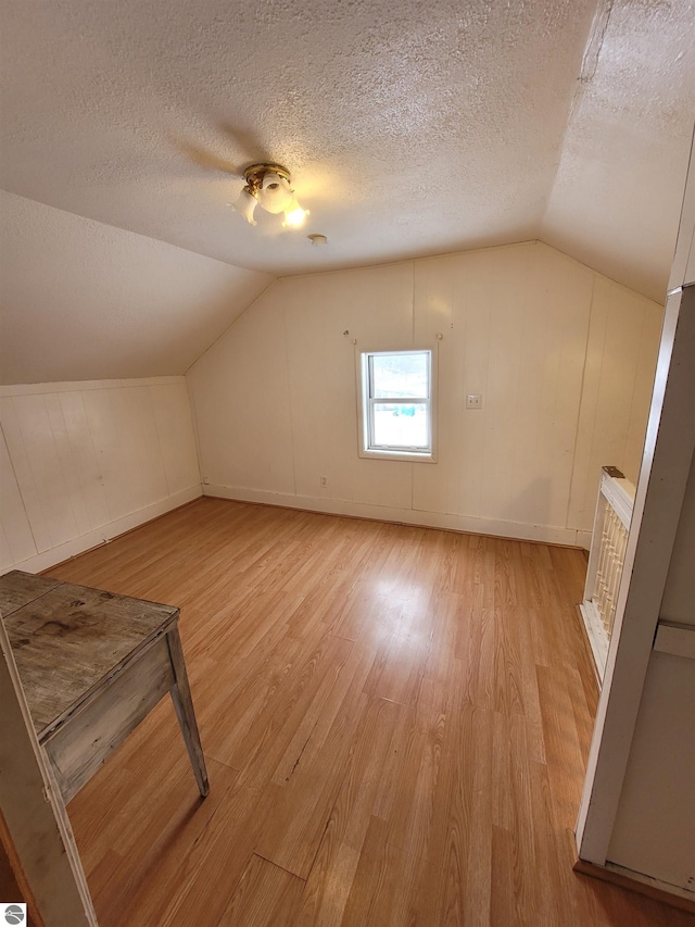 additional living space with light hardwood / wood-style floors, a textured ceiling, and vaulted ceiling