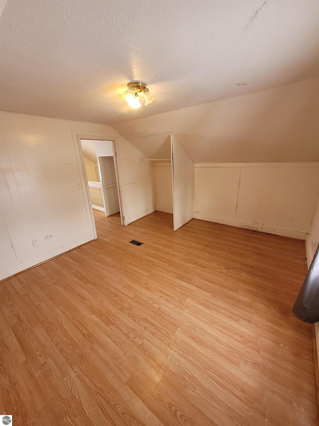 additional living space with lofted ceiling, light wood-type flooring, and a textured ceiling