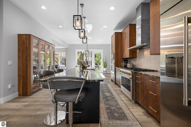 kitchen with sink, high end appliances, wall chimney range hood, and hanging light fixtures