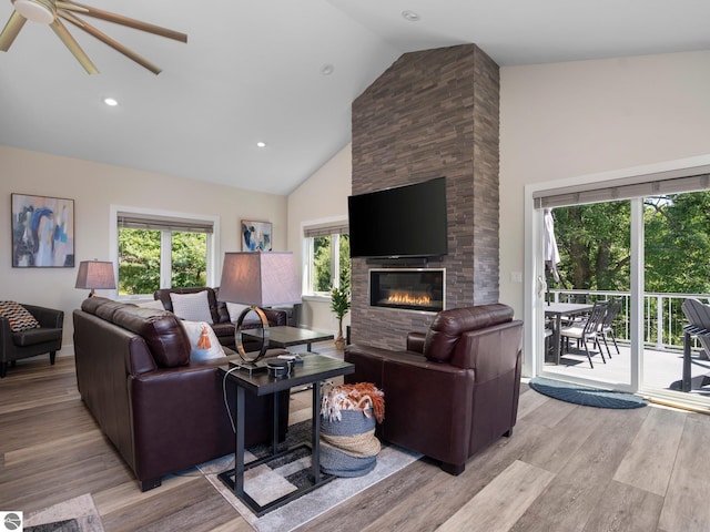 living room featuring high vaulted ceiling, light wood-type flooring, ceiling fan, and a stone fireplace