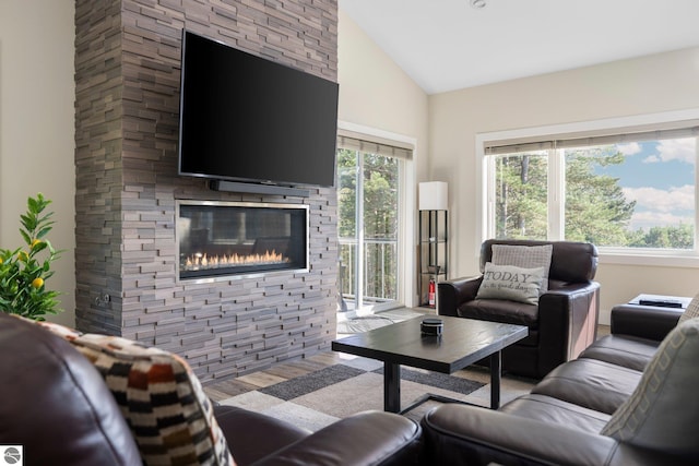 living room featuring vaulted ceiling, light hardwood / wood-style flooring, and a stone fireplace