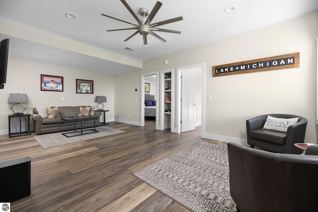 living room featuring ceiling fan, built in shelves, and dark wood-type flooring