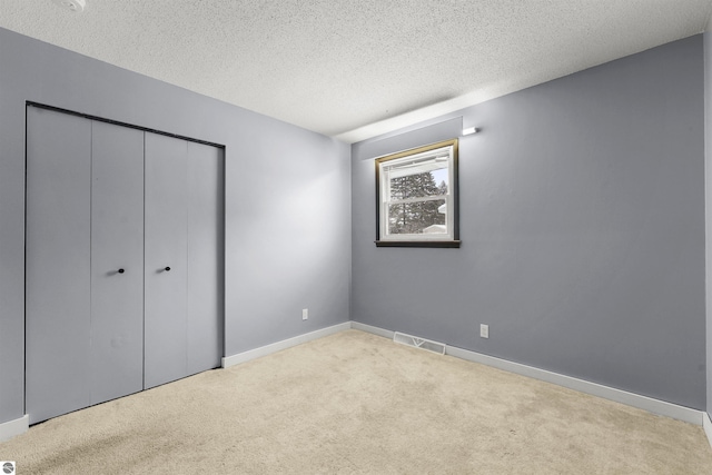 unfurnished bedroom featuring a textured ceiling, light colored carpet, and a closet