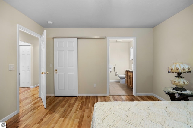 unfurnished bedroom featuring ensuite bathroom, a closet, and light hardwood / wood-style flooring