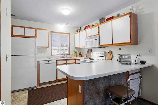 kitchen with white appliances, kitchen peninsula, white cabinetry, light tile patterned flooring, and sink