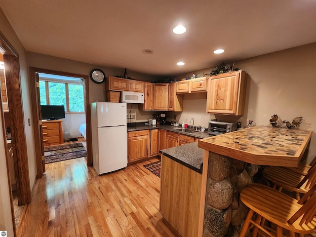 kitchen featuring white appliances, a breakfast bar area, light wood-type flooring, kitchen peninsula, and sink