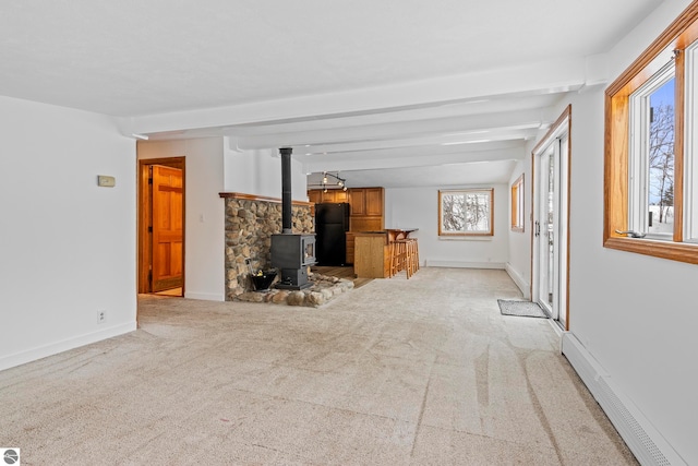 unfurnished living room featuring a baseboard heating unit, light carpet, a wood stove, and beamed ceiling