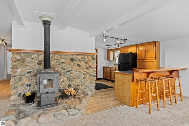 kitchen featuring kitchen peninsula, beamed ceiling, a kitchen breakfast bar, a wood stove, and black refrigerator