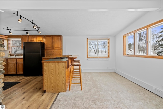 kitchen with black refrigerator, a baseboard heating unit, a breakfast bar area, lofted ceiling, and sink