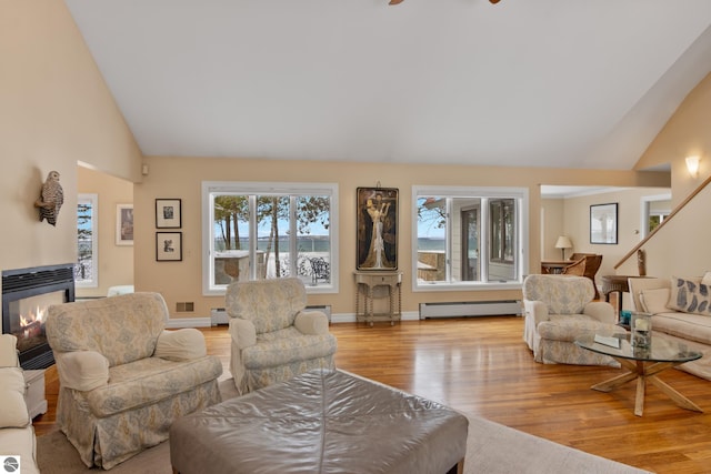 living room with lofted ceiling, a multi sided fireplace, baseboard heating, and light hardwood / wood-style flooring