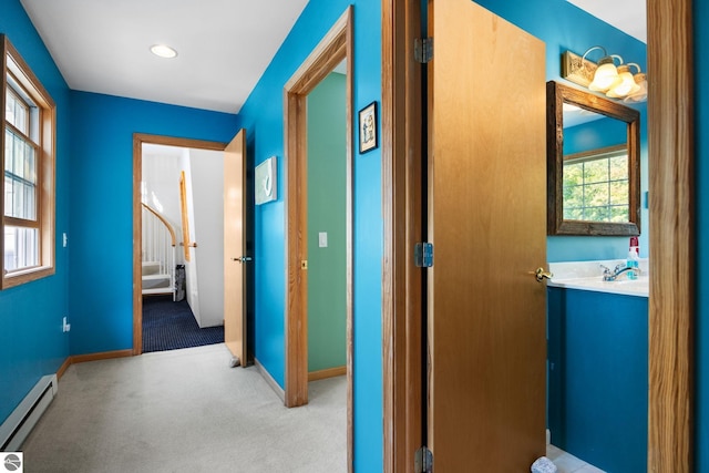 hall featuring a baseboard heating unit, light carpet, and a healthy amount of sunlight