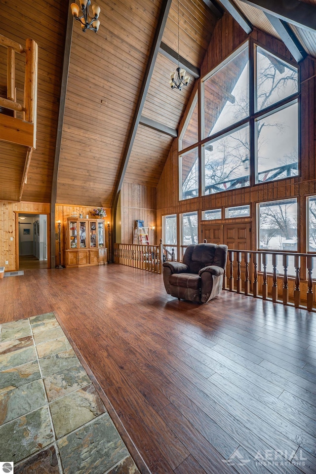 unfurnished living room with high vaulted ceiling, wooden walls, a chandelier, and beam ceiling