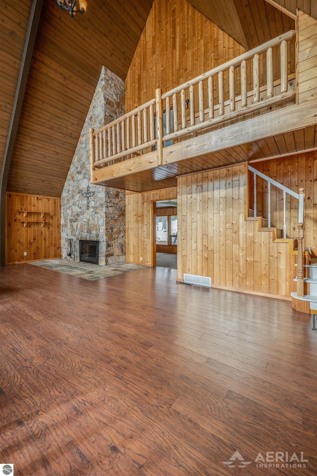 unfurnished living room featuring a fireplace, high vaulted ceiling, wooden walls, and wood-type flooring