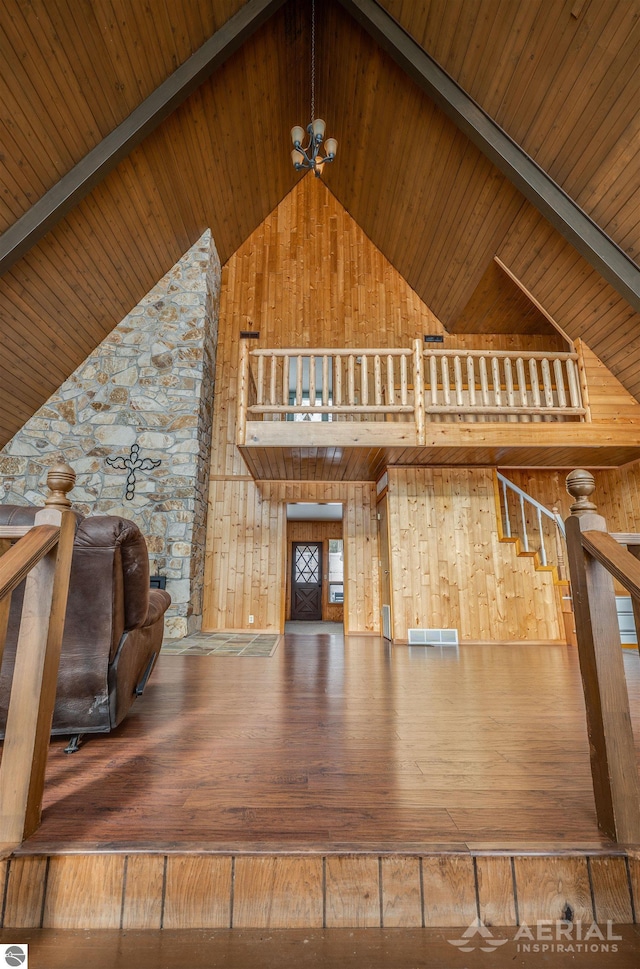 unfurnished living room with hardwood / wood-style flooring, a notable chandelier, wooden walls, high vaulted ceiling, and beamed ceiling