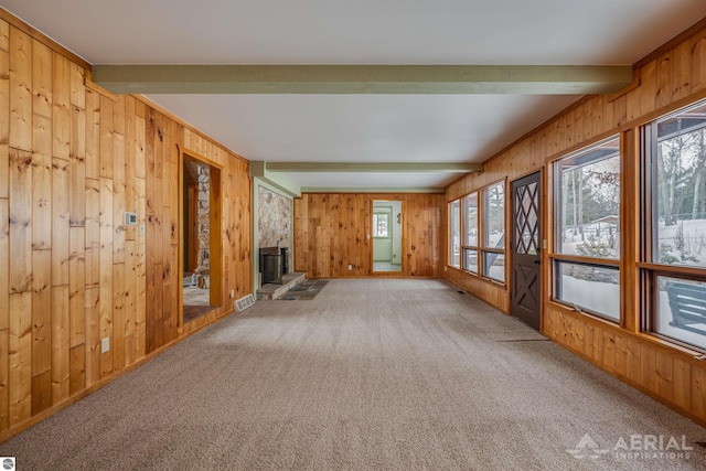 unfurnished living room featuring a fireplace, wooden walls, beamed ceiling, and carpet