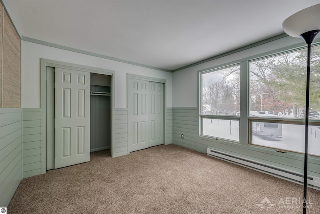 unfurnished bedroom featuring a baseboard heating unit, two closets, wooden walls, and carpet