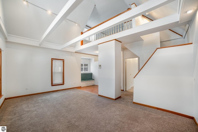 interior space with light colored carpet, beamed ceiling, a high ceiling, and track lighting