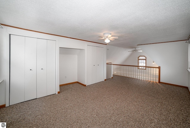 unfurnished bedroom with a textured ceiling, ceiling fan, carpet, and multiple closets