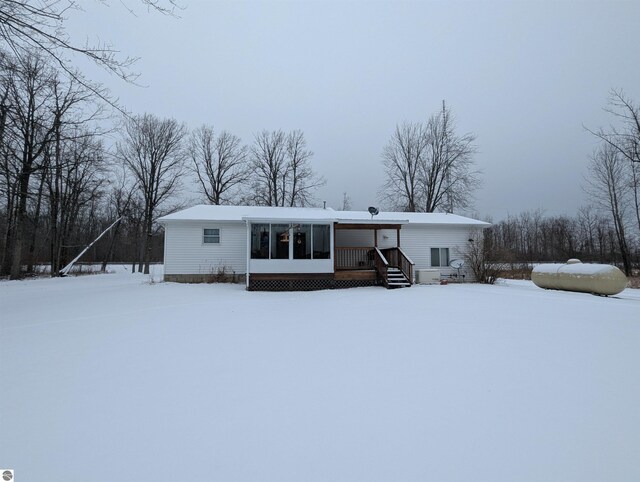 snow covered back of property featuring a sunroom