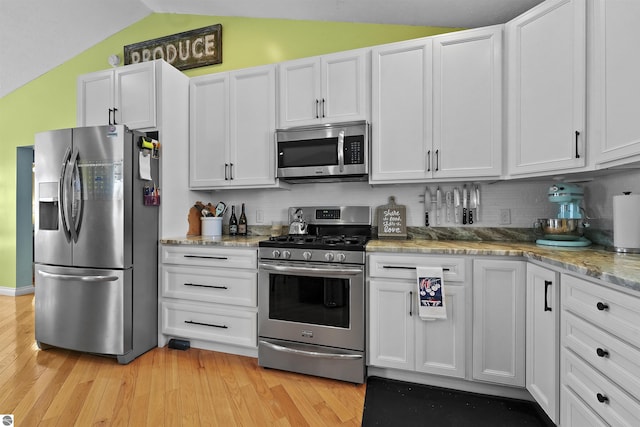 kitchen with light stone countertops, white cabinetry, stainless steel appliances, tasteful backsplash, and vaulted ceiling