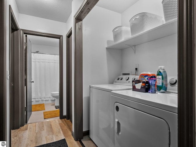 laundry area featuring a textured ceiling, washer and clothes dryer, and light hardwood / wood-style flooring