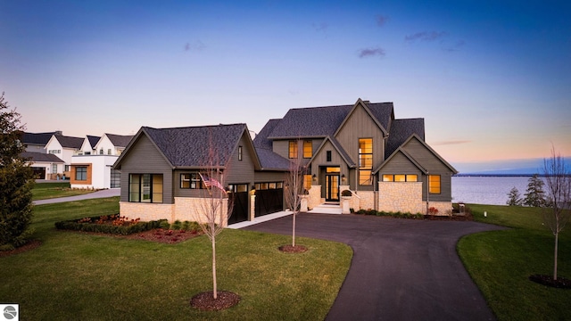 modern farmhouse with a garage, a water view, aphalt driveway, and a yard