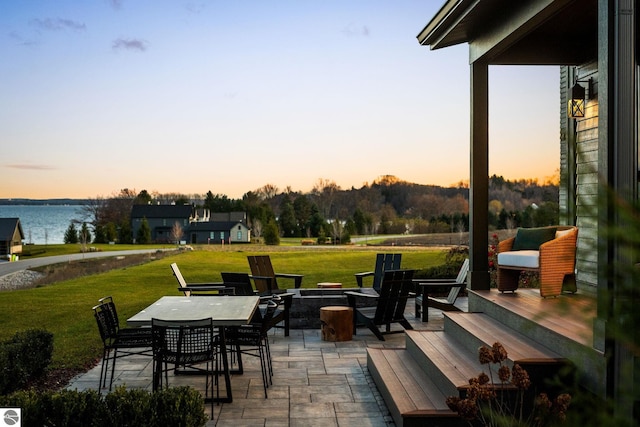 patio terrace at dusk featuring a water view and a yard