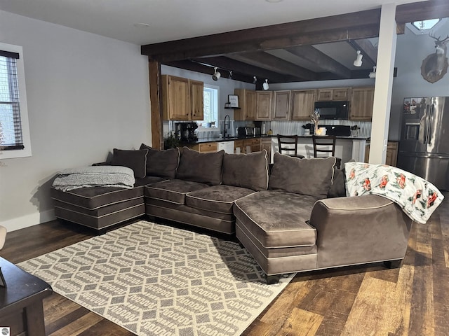 living room featuring dark wood-type flooring, sink, beamed ceiling, and rail lighting