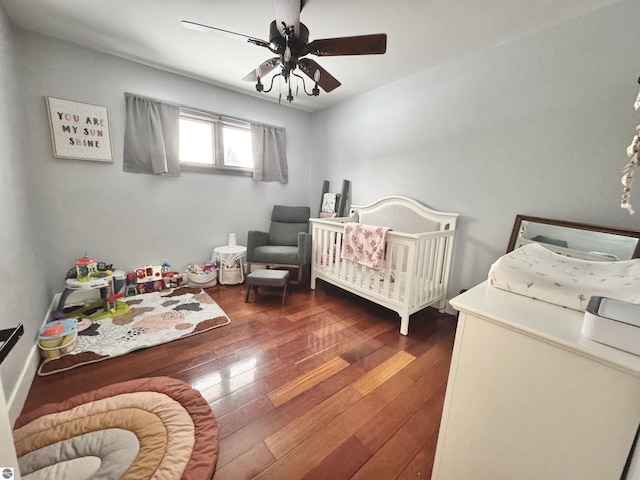 bedroom with ceiling fan, a nursery area, and dark hardwood / wood-style flooring