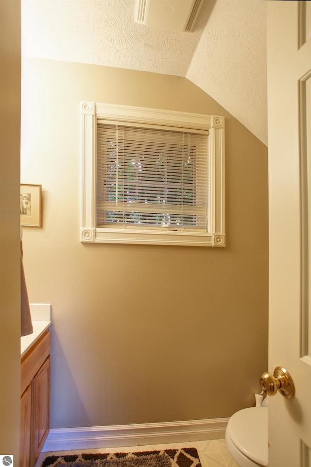 bathroom featuring a textured ceiling, toilet, vanity, and vaulted ceiling