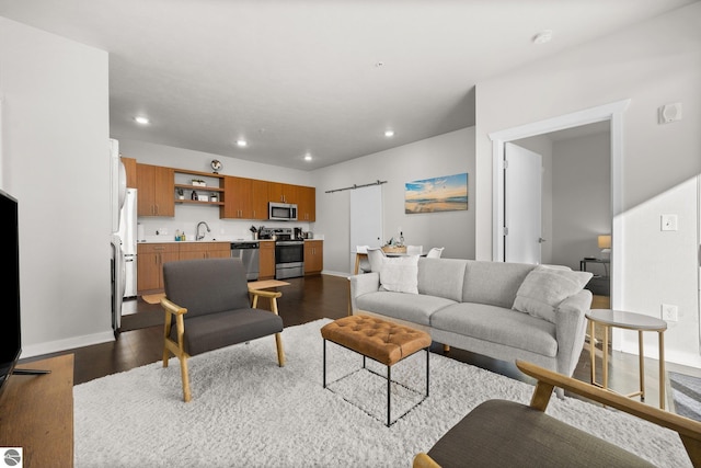 living room with a barn door, dark wood-type flooring, and sink