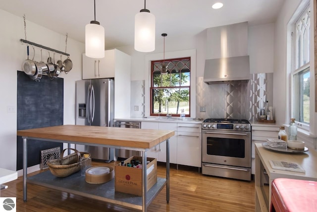 kitchen featuring pendant lighting, decorative backsplash, appliances with stainless steel finishes, white cabinets, and wall chimney exhaust hood