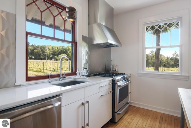 kitchen featuring white cabinets, wall chimney exhaust hood, stainless steel appliances, sink, and hanging light fixtures