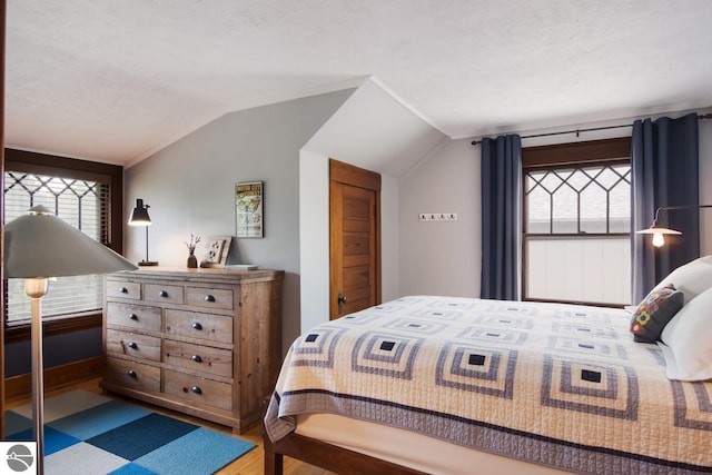 bedroom featuring wood-type flooring, multiple windows, a textured ceiling, and vaulted ceiling