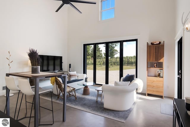 living room featuring ceiling fan, a towering ceiling, and concrete floors