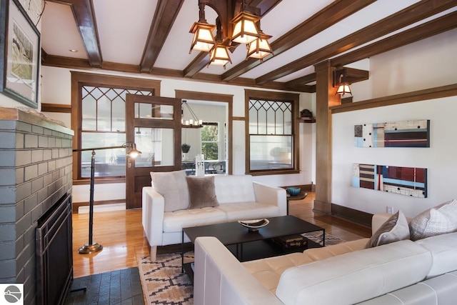 living room featuring a brick fireplace, wood-type flooring, beam ceiling, and a notable chandelier