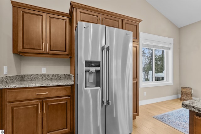 kitchen featuring light wood-type flooring, light stone countertops, vaulted ceiling, and high quality fridge