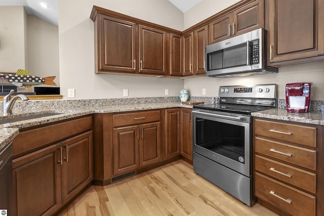 kitchen featuring lofted ceiling, stainless steel appliances, sink, light stone counters, and light hardwood / wood-style flooring