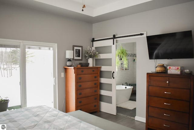 bedroom with dark wood-type flooring, ensuite bathroom, and a barn door