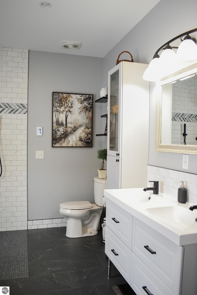 bathroom with toilet, vanity, backsplash, and a tile shower