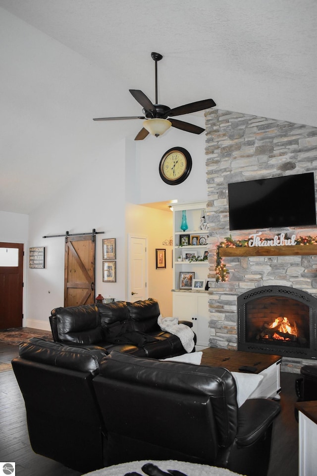 living room featuring lofted ceiling, a barn door, ceiling fan, a fireplace, and hardwood / wood-style flooring