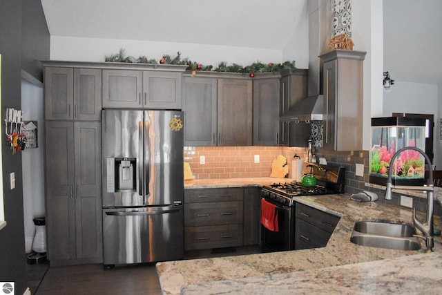 kitchen with stainless steel refrigerator with ice dispenser, decorative backsplash, black gas range oven, light stone counters, and sink