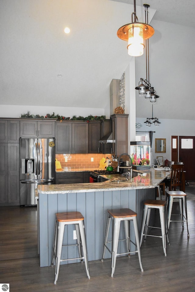 kitchen with kitchen peninsula, stainless steel refrigerator with ice dispenser, decorative backsplash, decorative light fixtures, and vaulted ceiling