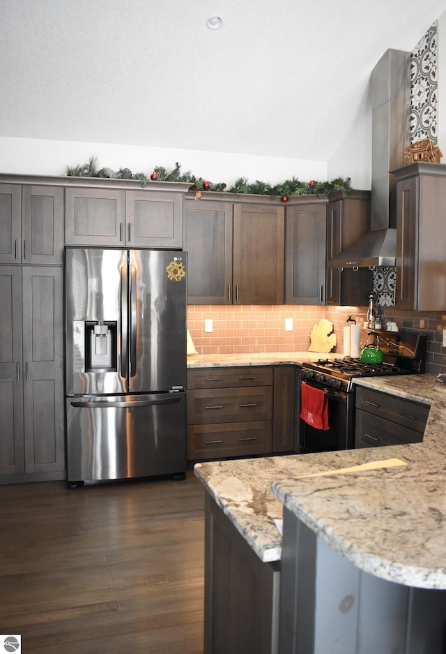 kitchen featuring stainless steel fridge, lofted ceiling, wall chimney range hood, light stone countertops, and black gas stove