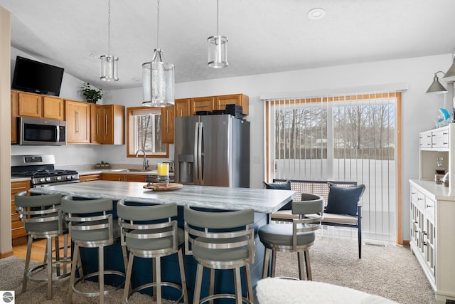 kitchen featuring decorative light fixtures, carpet, appliances with stainless steel finishes, and a kitchen island