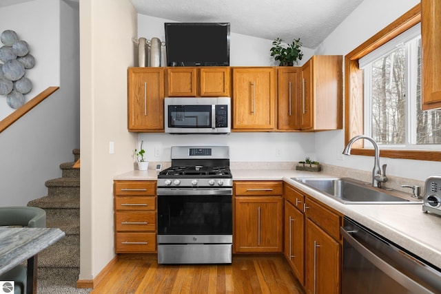 kitchen with a textured ceiling, appliances with stainless steel finishes, light hardwood / wood-style floors, and sink